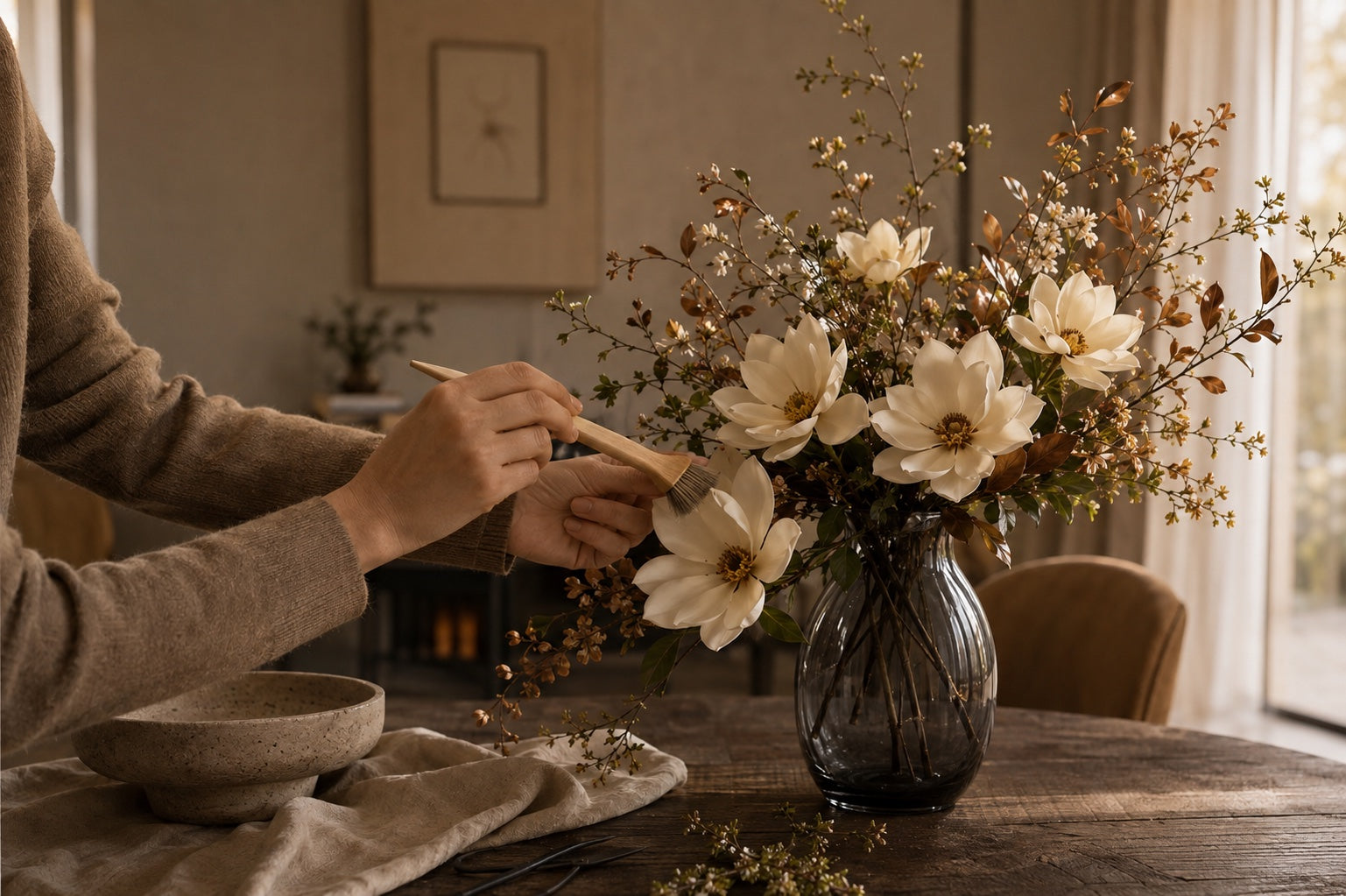 A soft brush cleaning an ivory faux magnolia while the stem is supported by hand